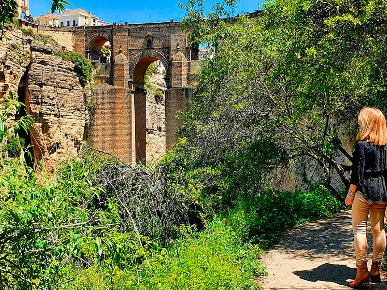 Visitante caminando hacia el Puente Nuevo de Ronda entre la vegetación